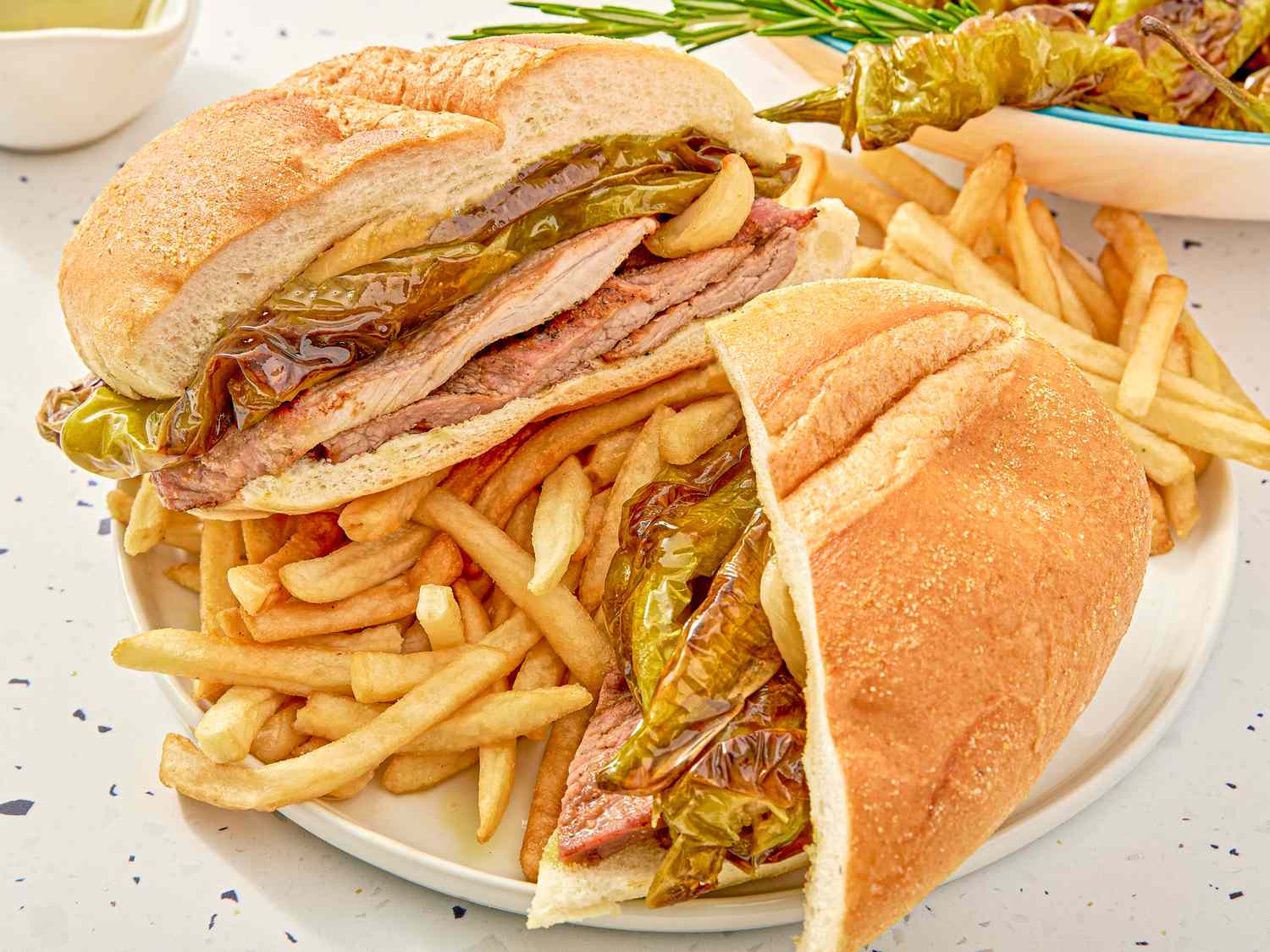 A sandwich filled with meat and peppers served with French fries on a plate