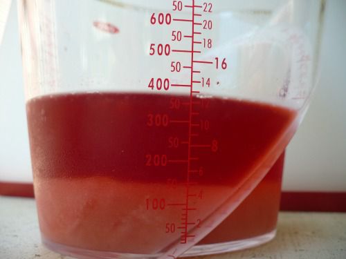 Undissolved sugar settled at the bottom of berry syrup mixture in measuring cup