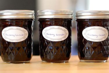 Profile view of three half-pint canning jars filled with lavender blueberry jam.