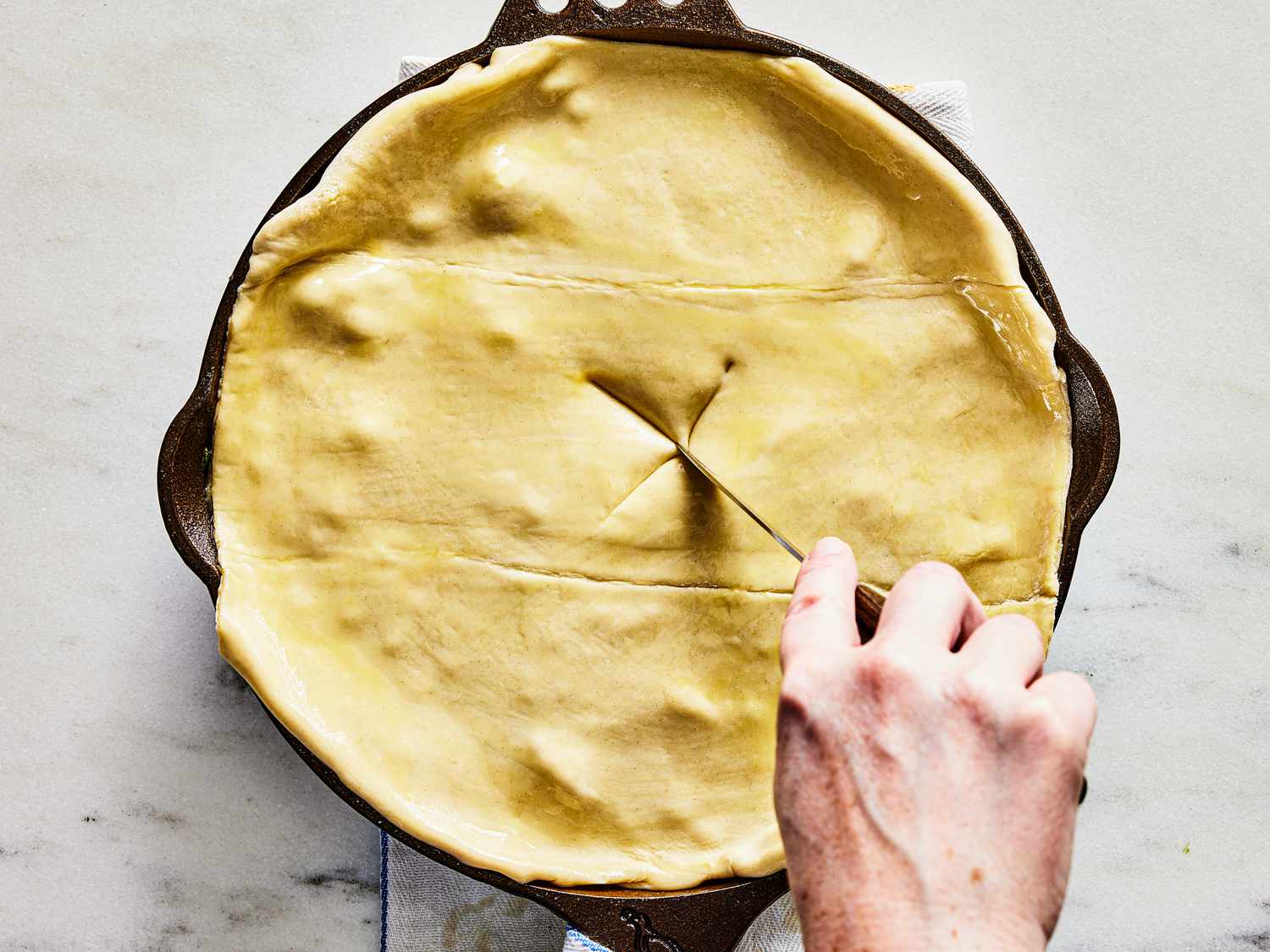 Cutting an "X" into center of pastry of pot pie in skillet 