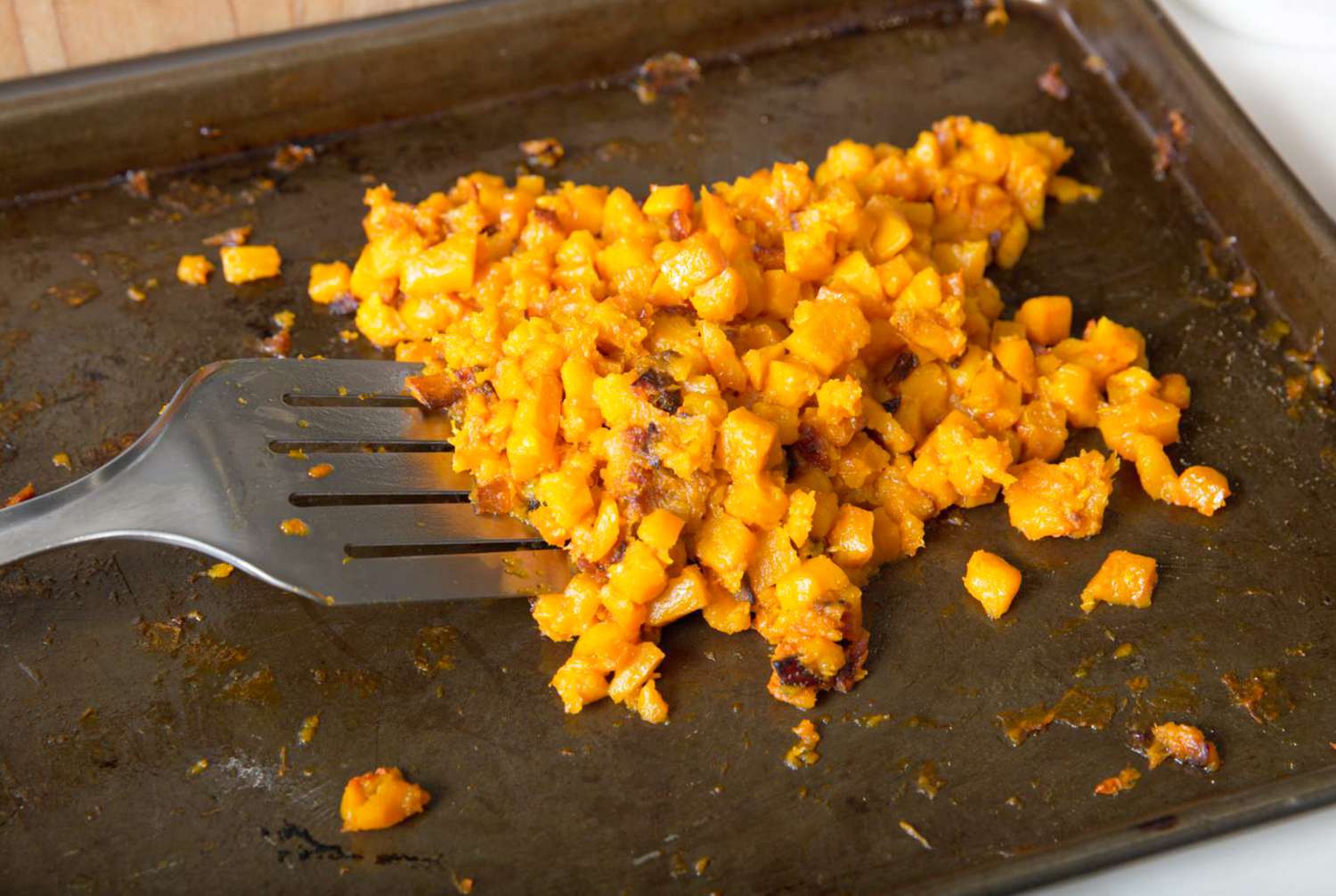 Roasted butternut squash scraped together on a sheetpan with the spatula 