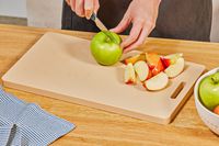 A person slicing apples on a plastic cutting board.