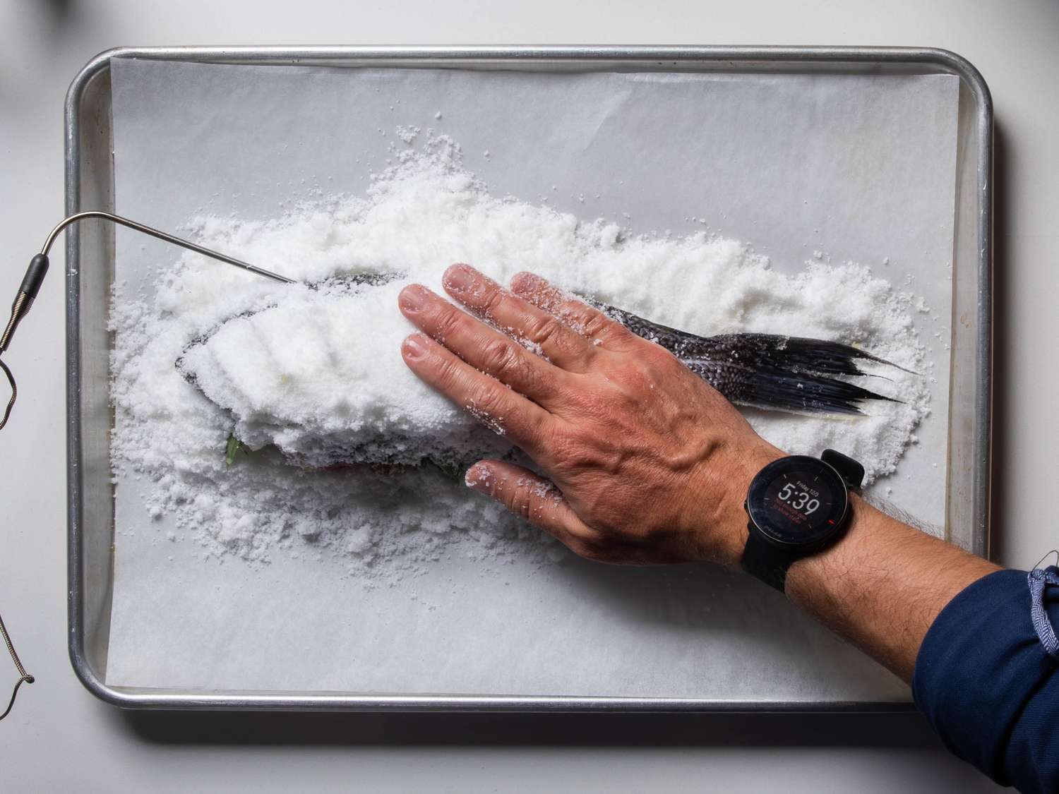 Packing salt around a whole fish that has a leave-in probe thermometer inserted into it already.