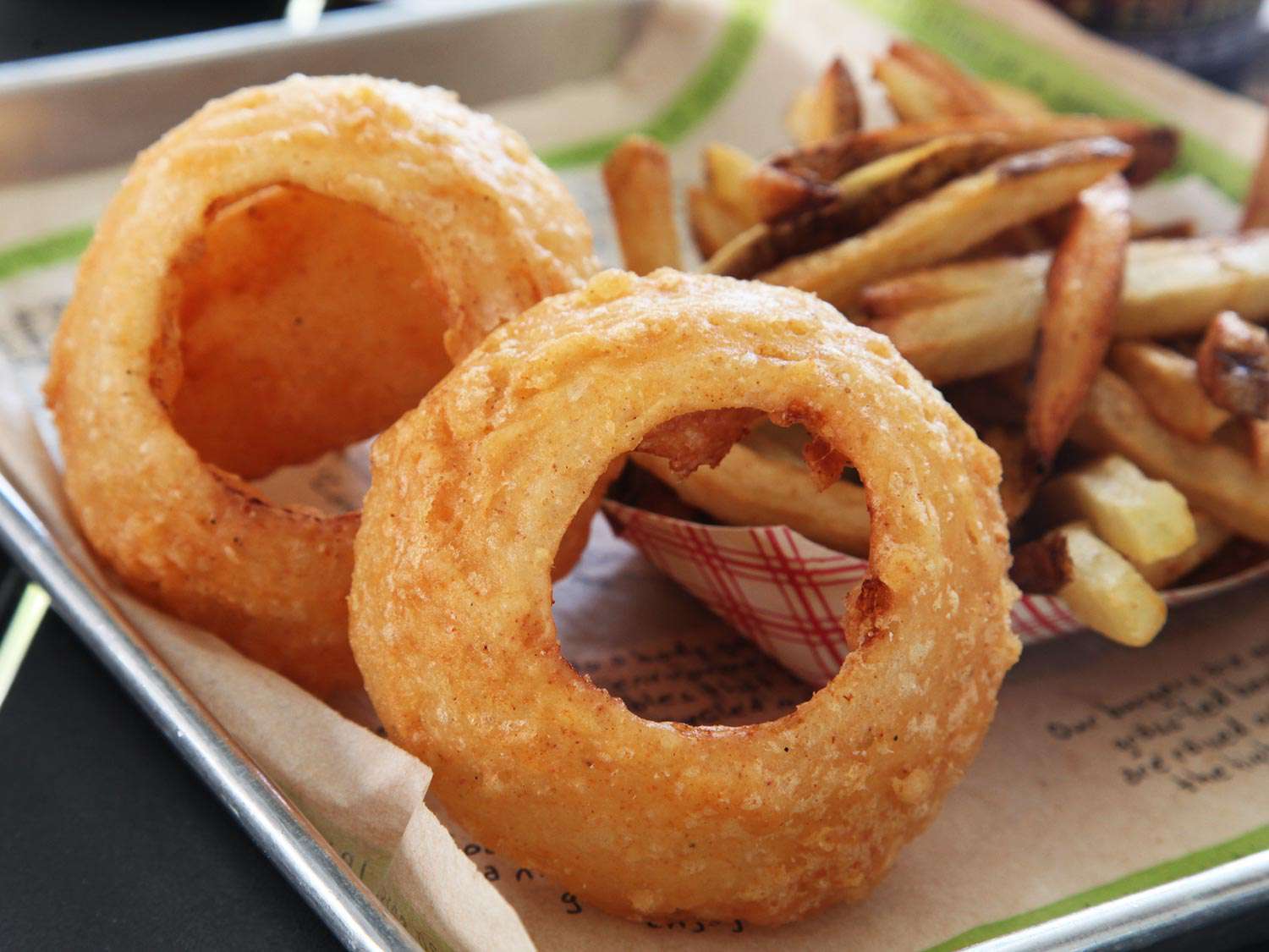 A serving tray with giant onion rings from Burger Fi and a paper container of french fries