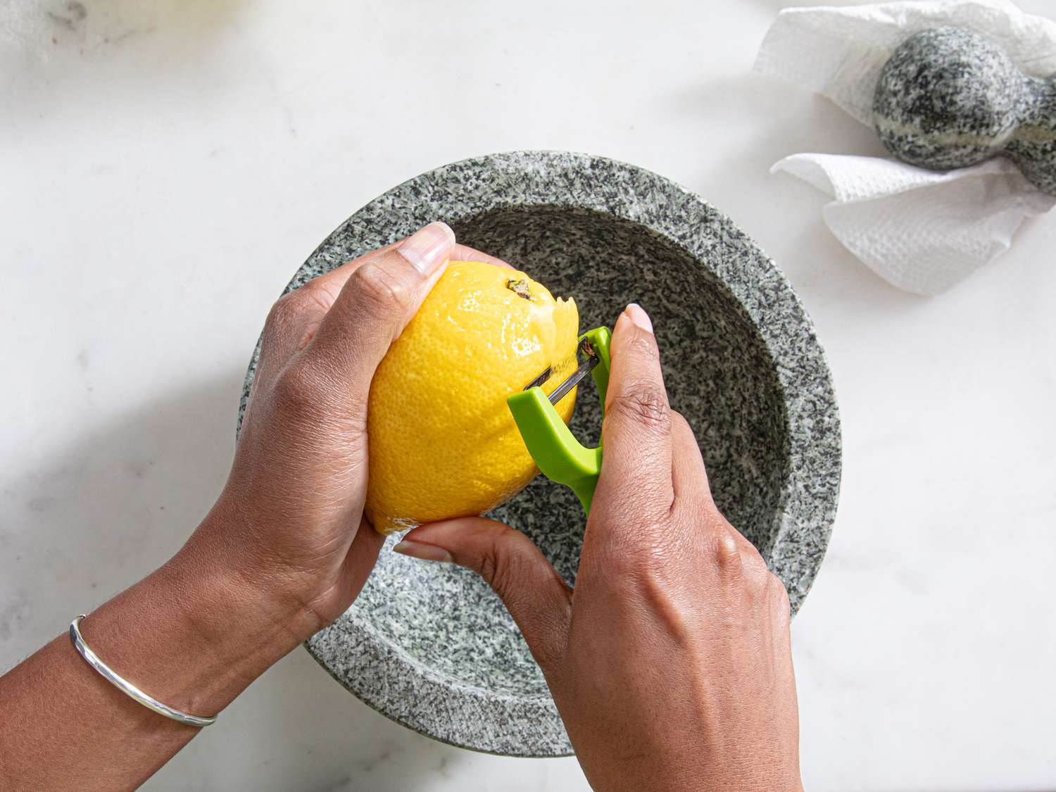 Using a peeler to remove the yellow peel from a lemon.
