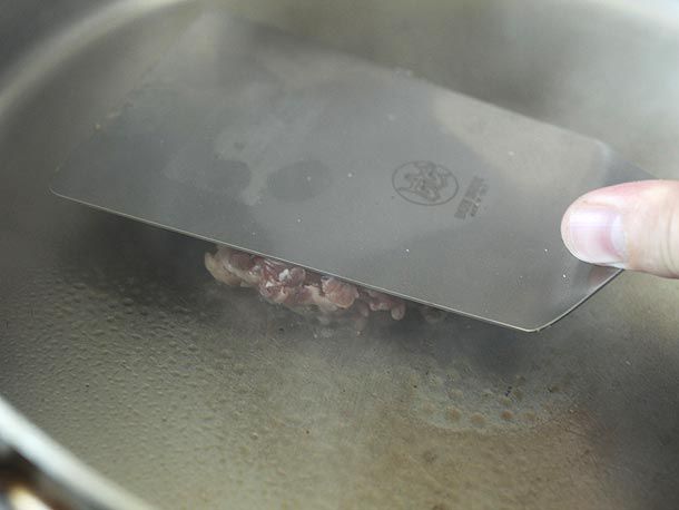 Smashing a hamburger patty in a smoking hot stainless steel skillet