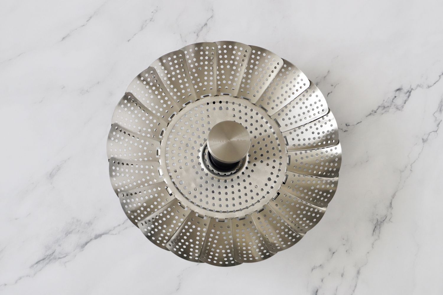 A stainless steel steamer basket on a marble surface