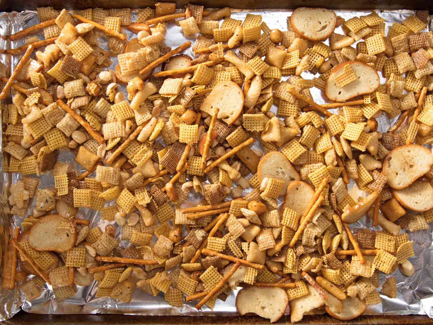 The butter-tossed chex mix spread evenly on a sheet pan lined with foil.