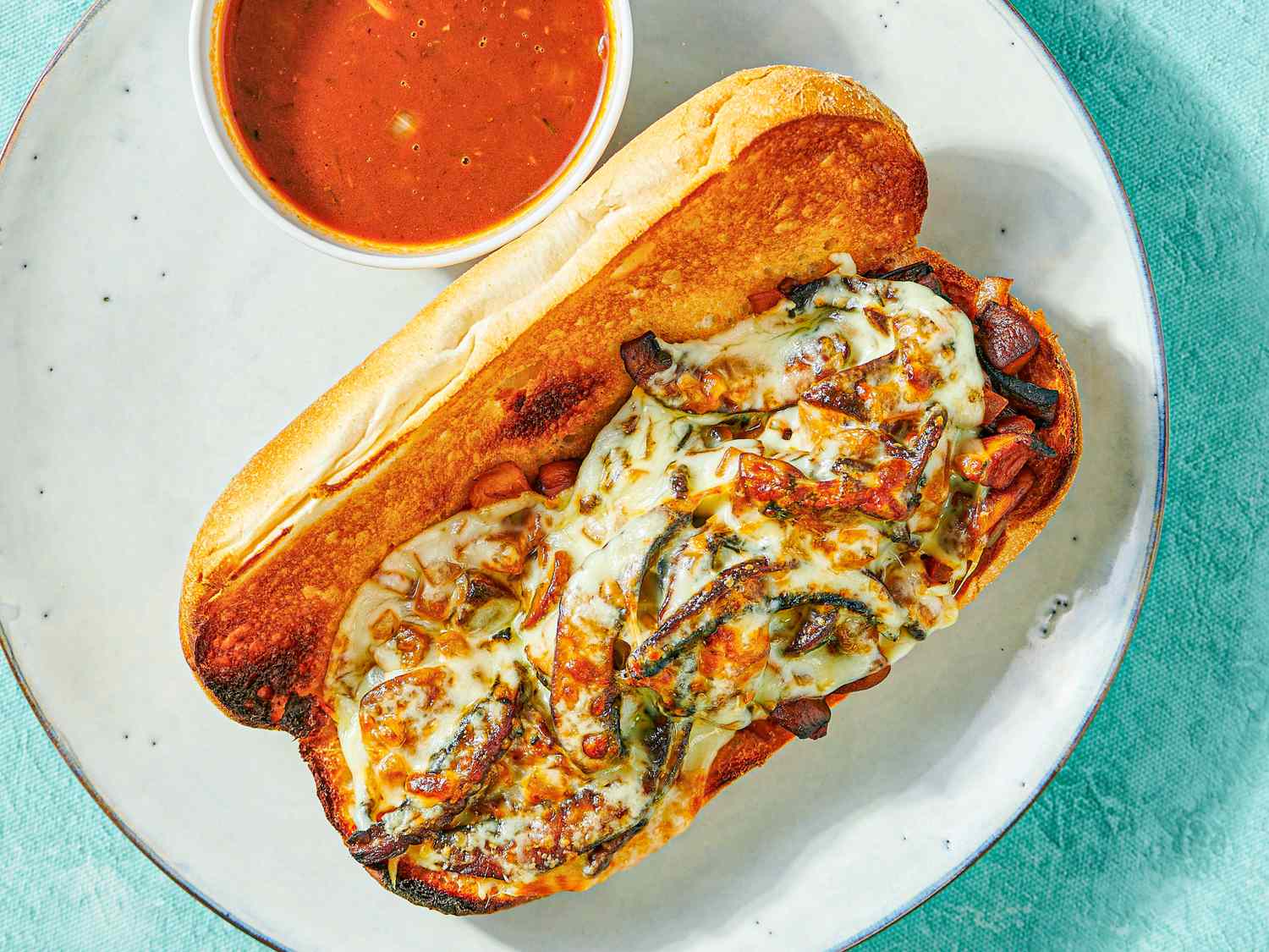 Vegetarian French dip sandwich with roasted vegetables and melted cheese, served with a side of dipping sauce