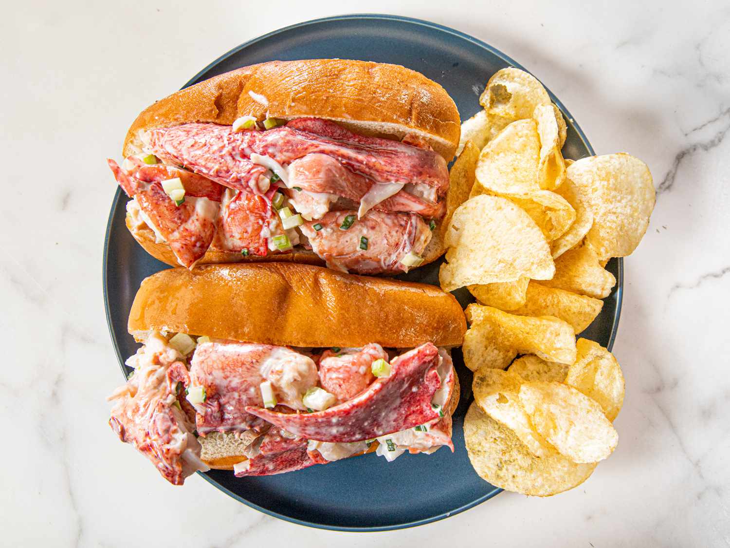 Two lobster rolls on a blue plate with potato chips 