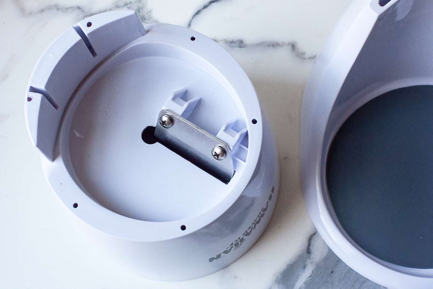 Interior view of a plastic container with a metal attachment of Hawaiian Shaved Ice HomePro Shave Ice and Snow Cone Machine (S777) piece, alongside its lid resting on a marble surface