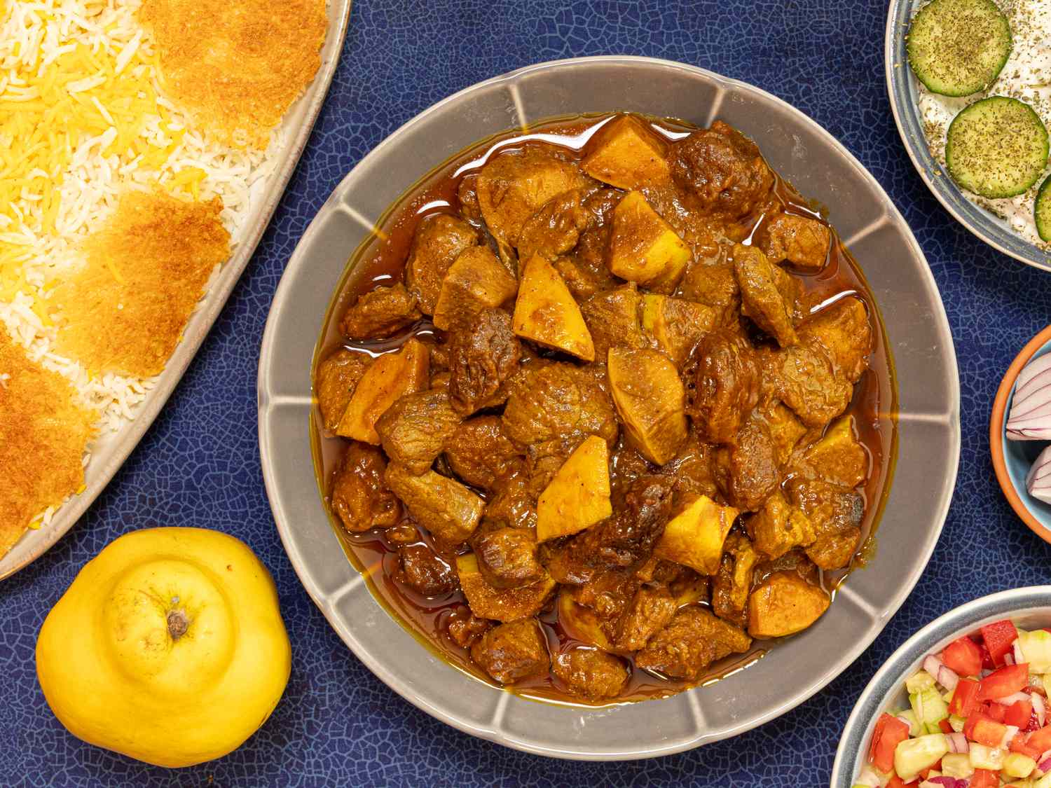 A dish of khoreshe beh alongside sides like rice and other accompaniments