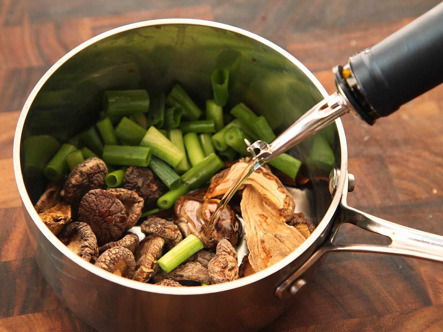 Dried mushrooms and chopped scallions in a saucepan with oil being added to make flavored oil topping for creamy vegan ramen.