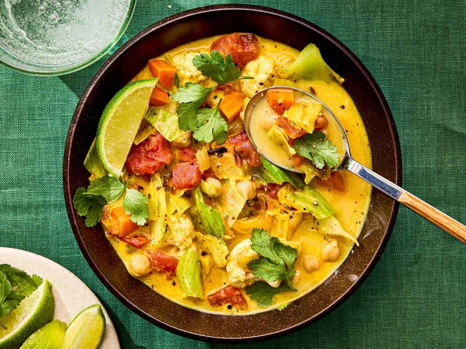 A bowl of cabbage soup with lime wedges and a spoon