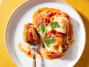 A plate with a zucchini parmesan dish garnished with basil accompanied by a fork