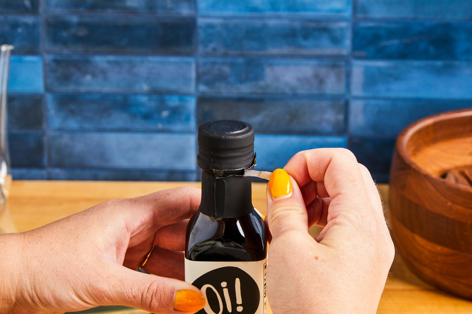 Hands opening a bottle by peeling off the seal surrounding its neck