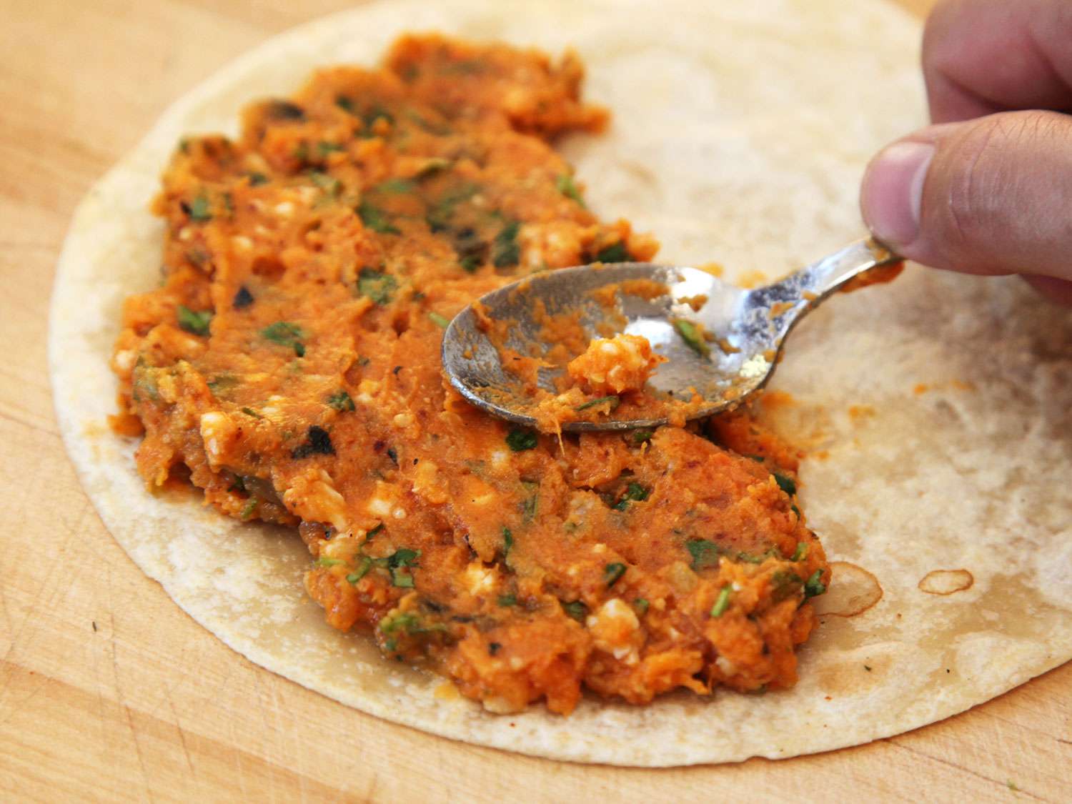 Spreading mashed sweet potatoes on a tortilla. 