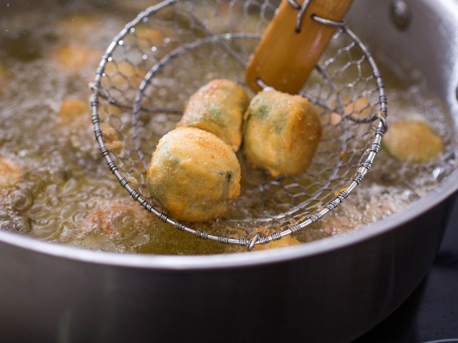 The golden, fried poppers are removed from the oil with a spider.