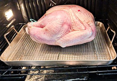 A turkey placed in an oven on a roasting pan with a rack