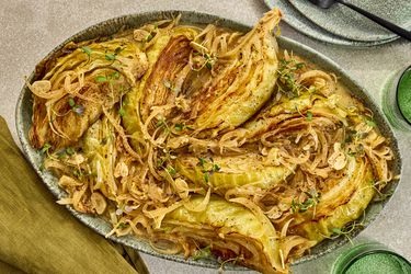 cabbage on a platter with plates, forks and green napkins, and cups on the sides