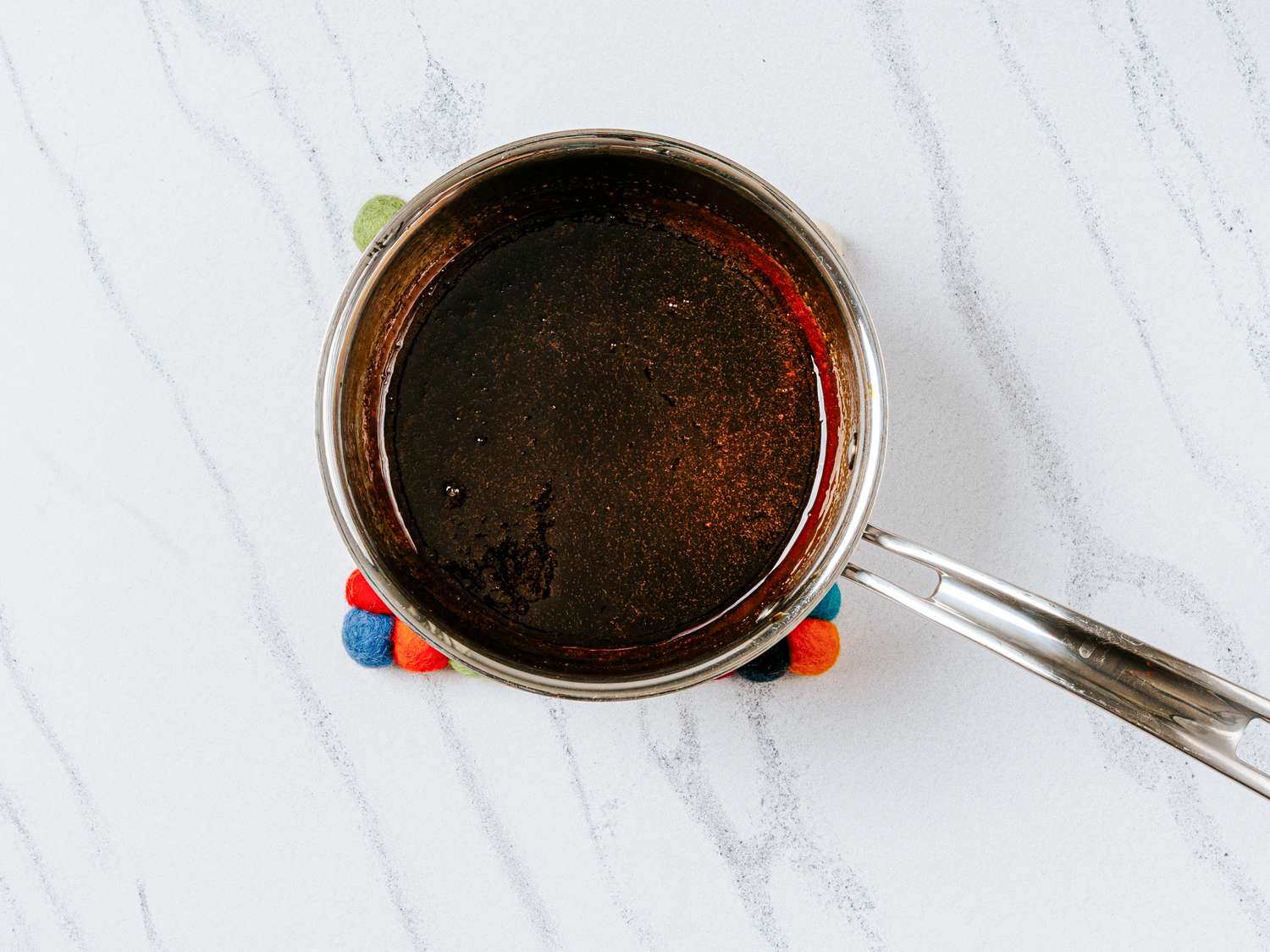 Small saucepan with dark liquid inside placed on colorful coaster on a marble surface