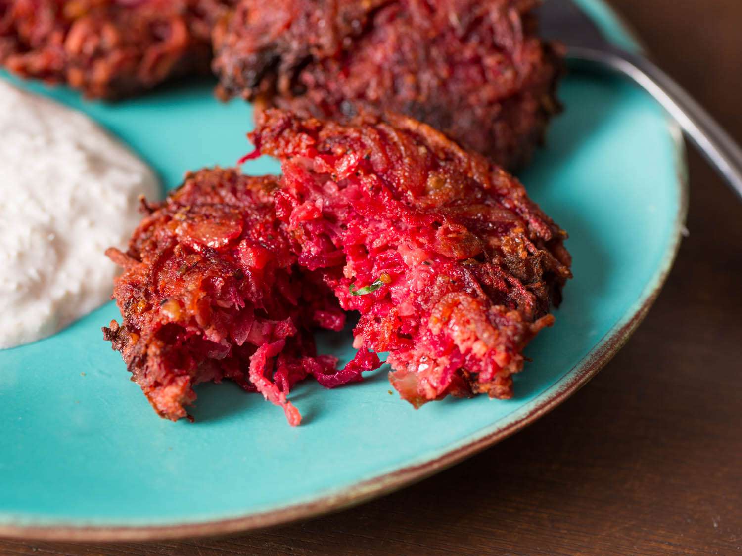 A small plate of beet latkes and horseradish sour cream sauce. One latke is torn in half. 