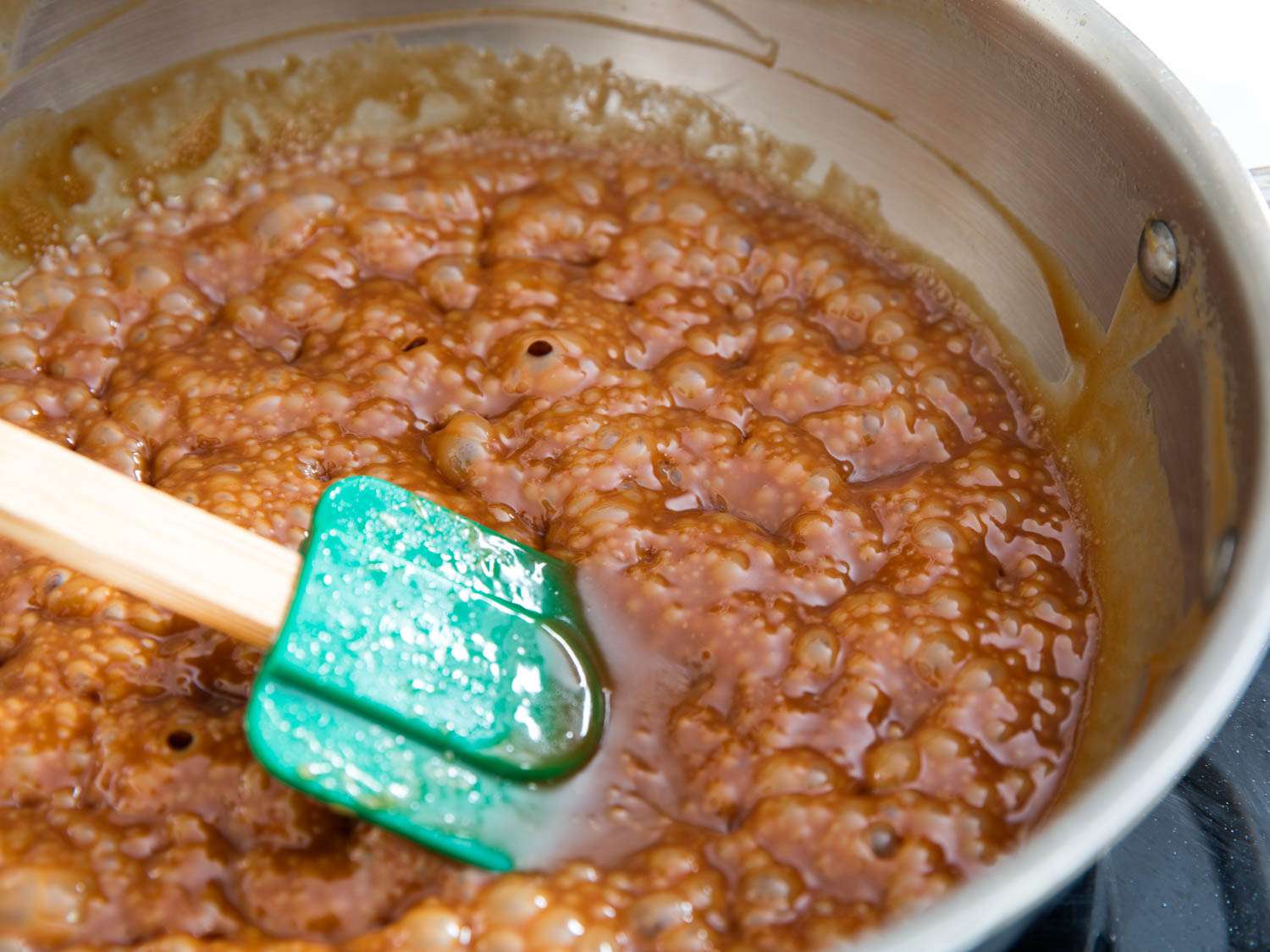 A flexible spatula stirring a pot of bubbling caramel