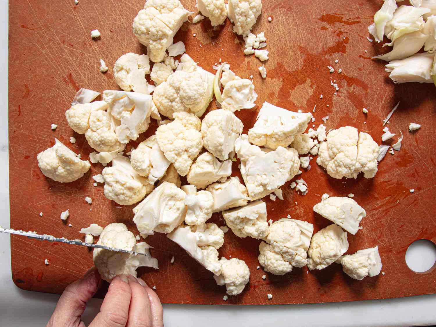 A hand cutting cauliflower on a wooden surface