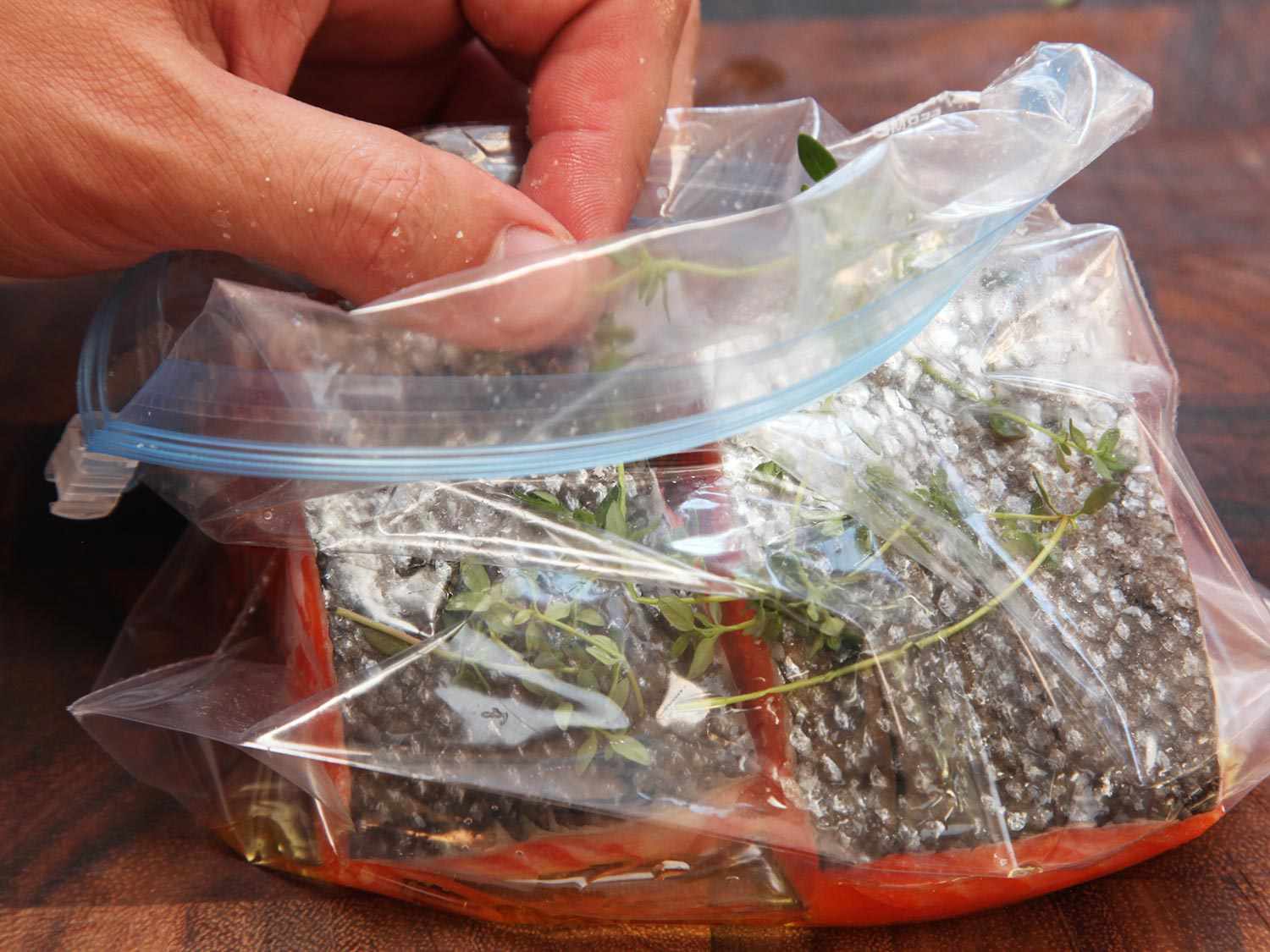 Adding thyme sprigs to a zipper lock bag containing two salmon fillets and olive oil before cooking sous vide.