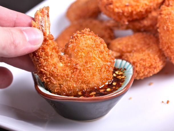 Closeup of a coconut shrimp being dipped into a small bowl of sauce.