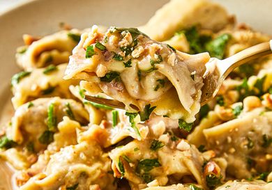 A closeup of a fork lifting a stuffed pasta piece from a dish of agnolotti with garnish