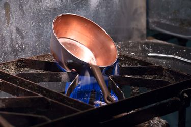 A copper pot heating on an open flame before tin is added to its interior.