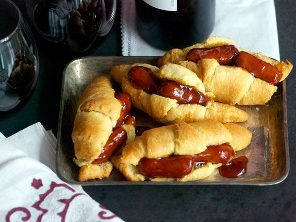 Four glazed cocktail sausage and crescent roll sandwiches, served on a small baking sheet.