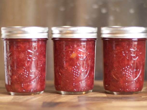 A row of three lidded glass jars of cranberry orange jam displayed on wooden surface