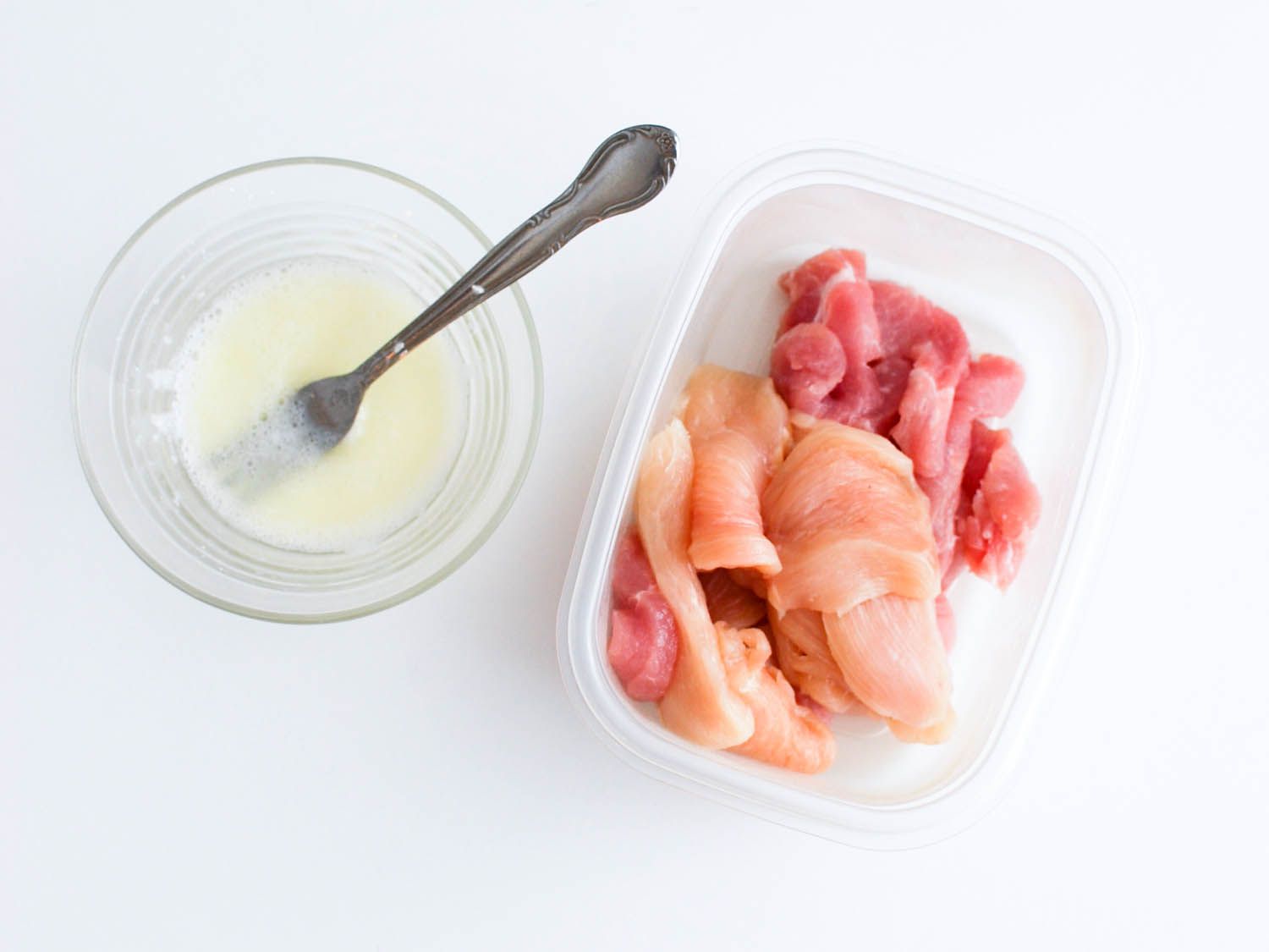 Pork, chicken, and cod fish in a plastic plastic dish with a marinade off to the side.