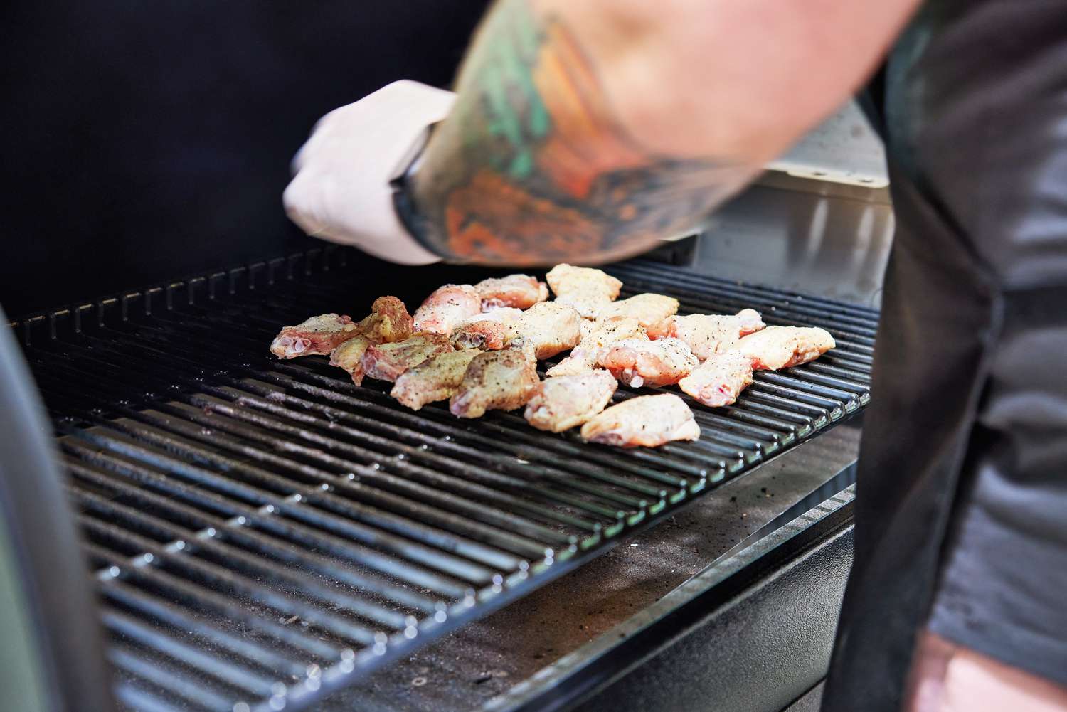 A hand placing uncooked chicken wings onto a Traeger's grill grates