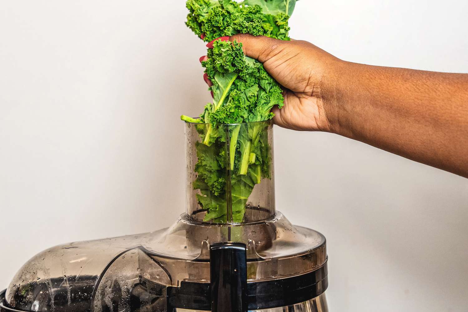 A person adding whole kale leaves to the food chute of a juicer