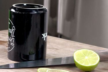 An upended coffee mug is set on a cutting board next to a chef's knife and a thinly sliced lime.