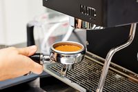 Hand holding the portafilter filled with coffee grounds next to the Diletta Mio Espresso Machine