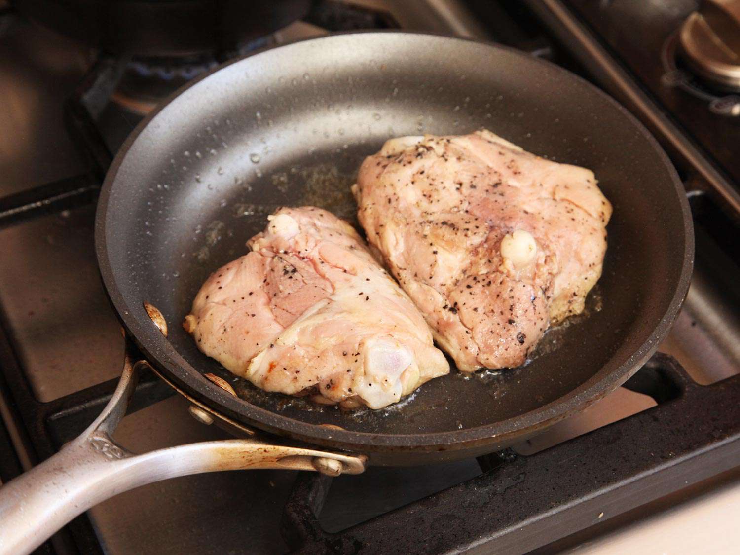 Two chicken thighs placed into a skillet to crisp after being cooked sous vide. 