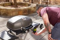 A person adding inserting the propane tank to a portable gas grill.