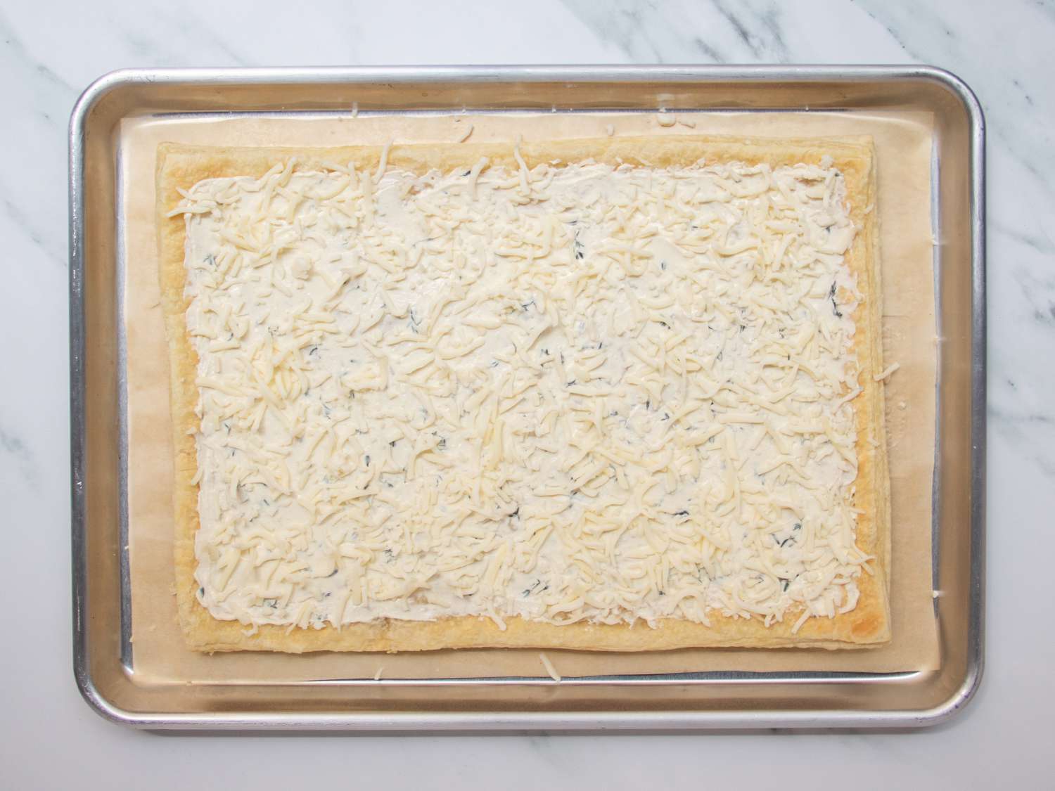 Par-baked puff pastry crust in a rimmed baking sheet, topped with seasoned cream cheese spread and mozzarella