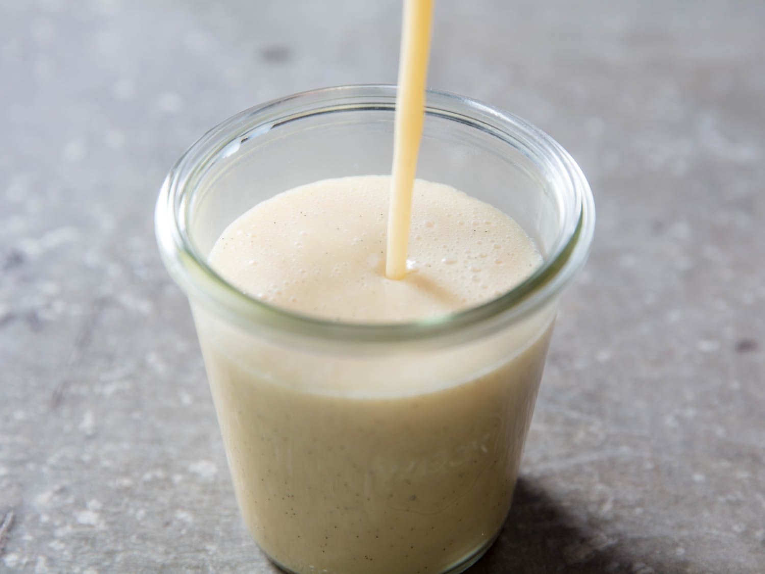 A stream of homemade sweetened condensed milk filling a clear glass jar