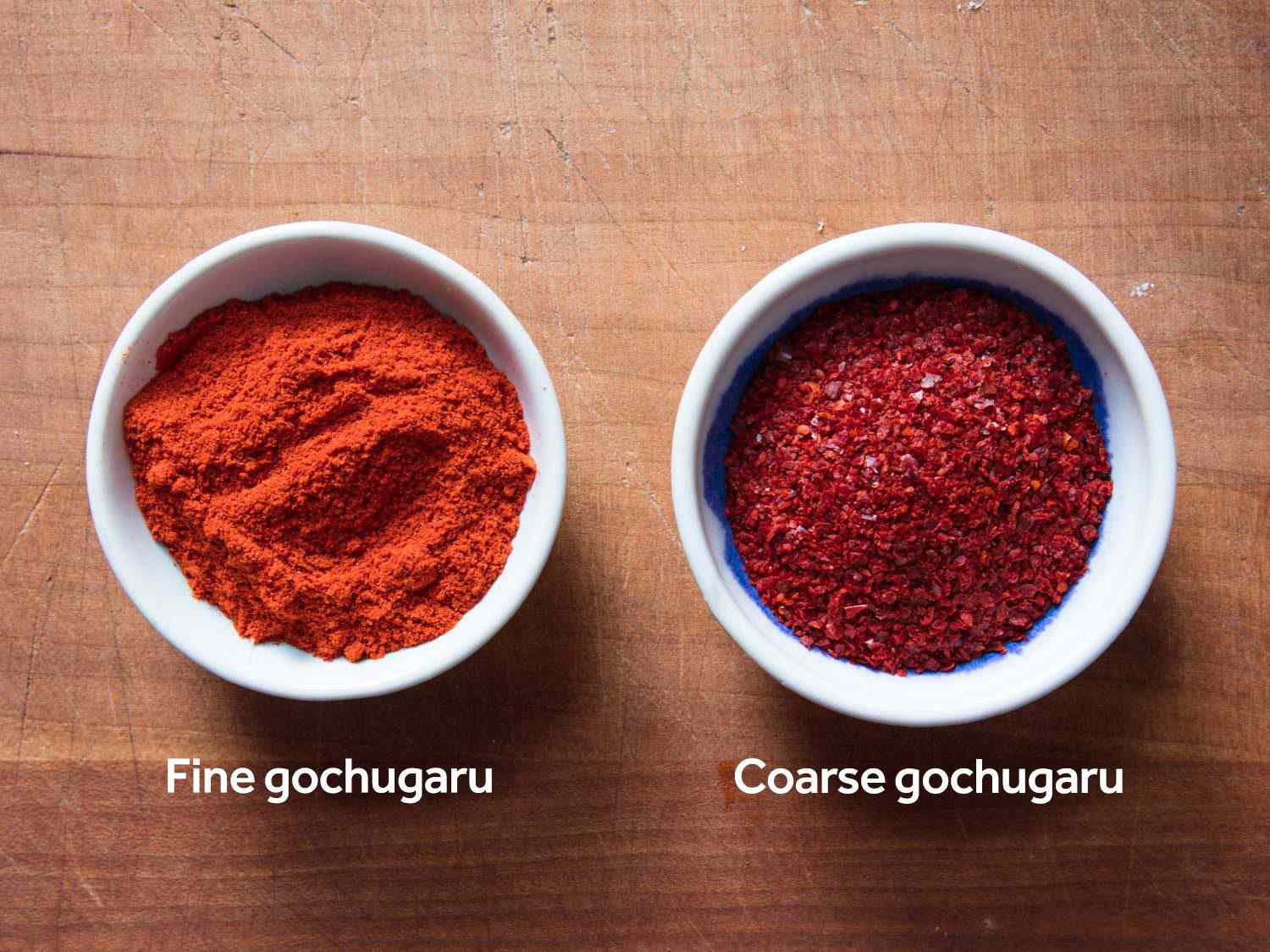 Side by side bowls filled with red Korean chile powders: fine gochugaru and coarse gochugaru.