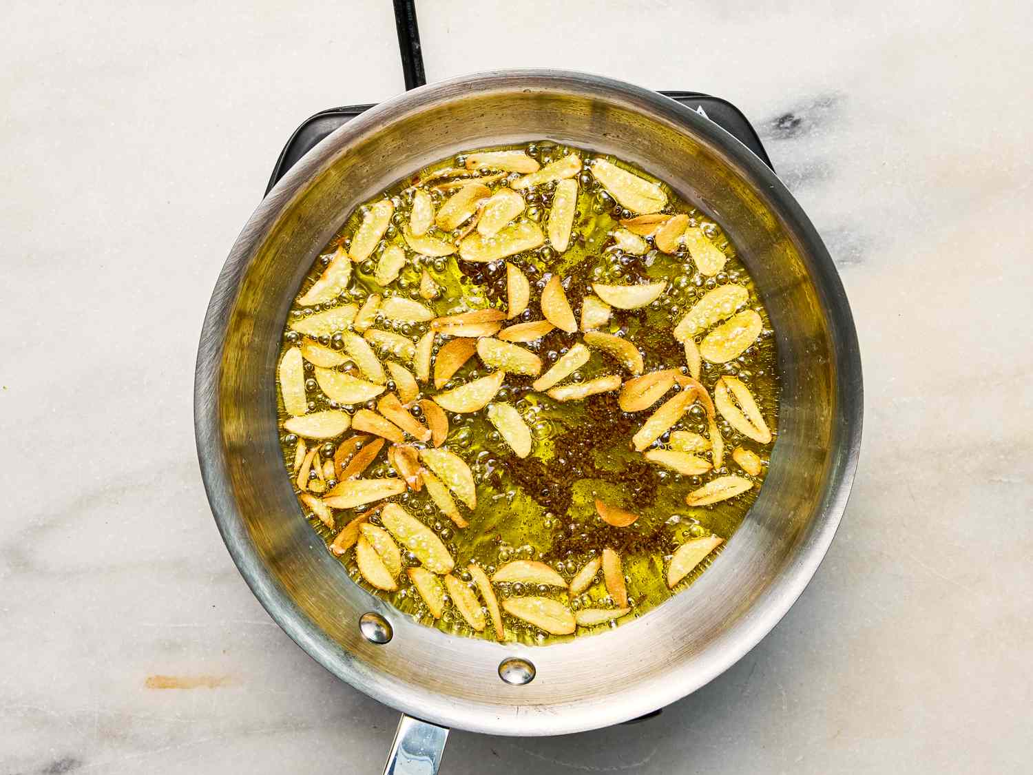 Sliced almonds frying in a pan of oil on a light surface preparation of ingredients for a dish