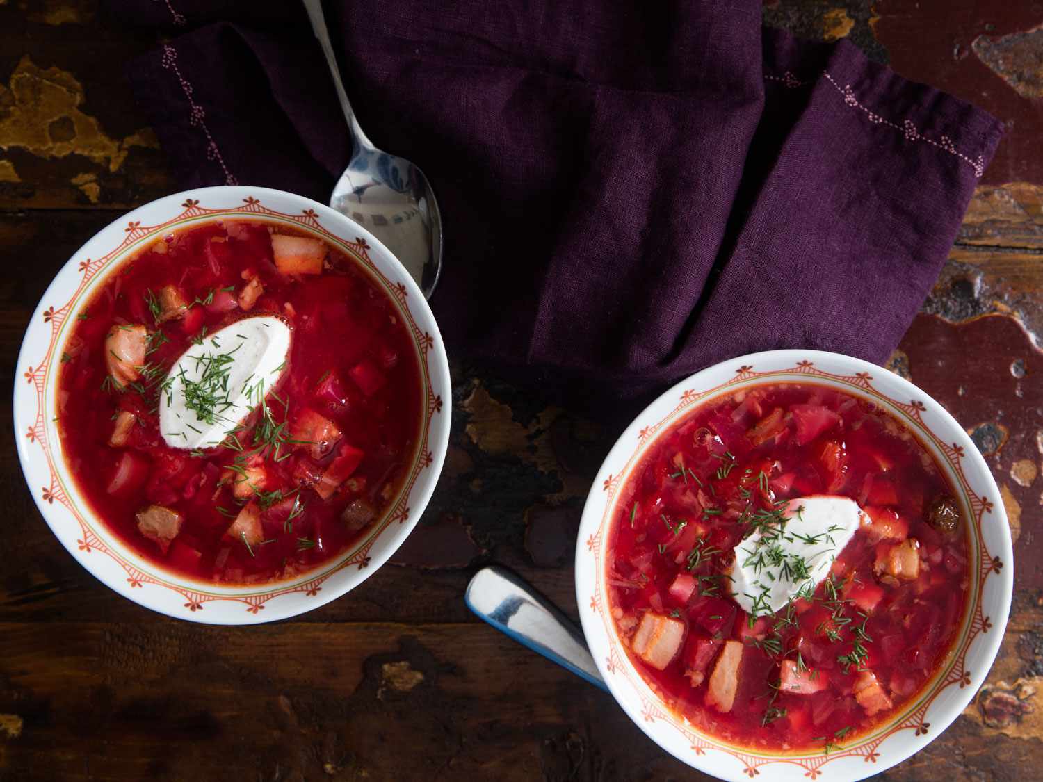 Overhead shot of two bowls of Ukrainian borscht topped with dollops of sour cream and fresh dill.