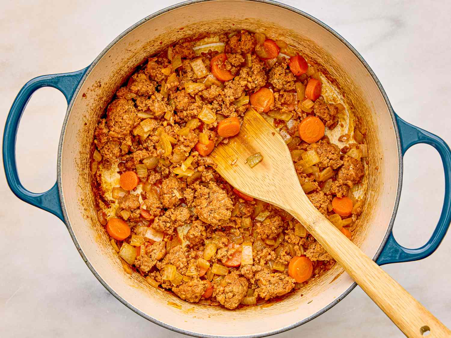 A pot with sausage lentils and diced vegetables being cooked a wooden spoon resting in the mixture