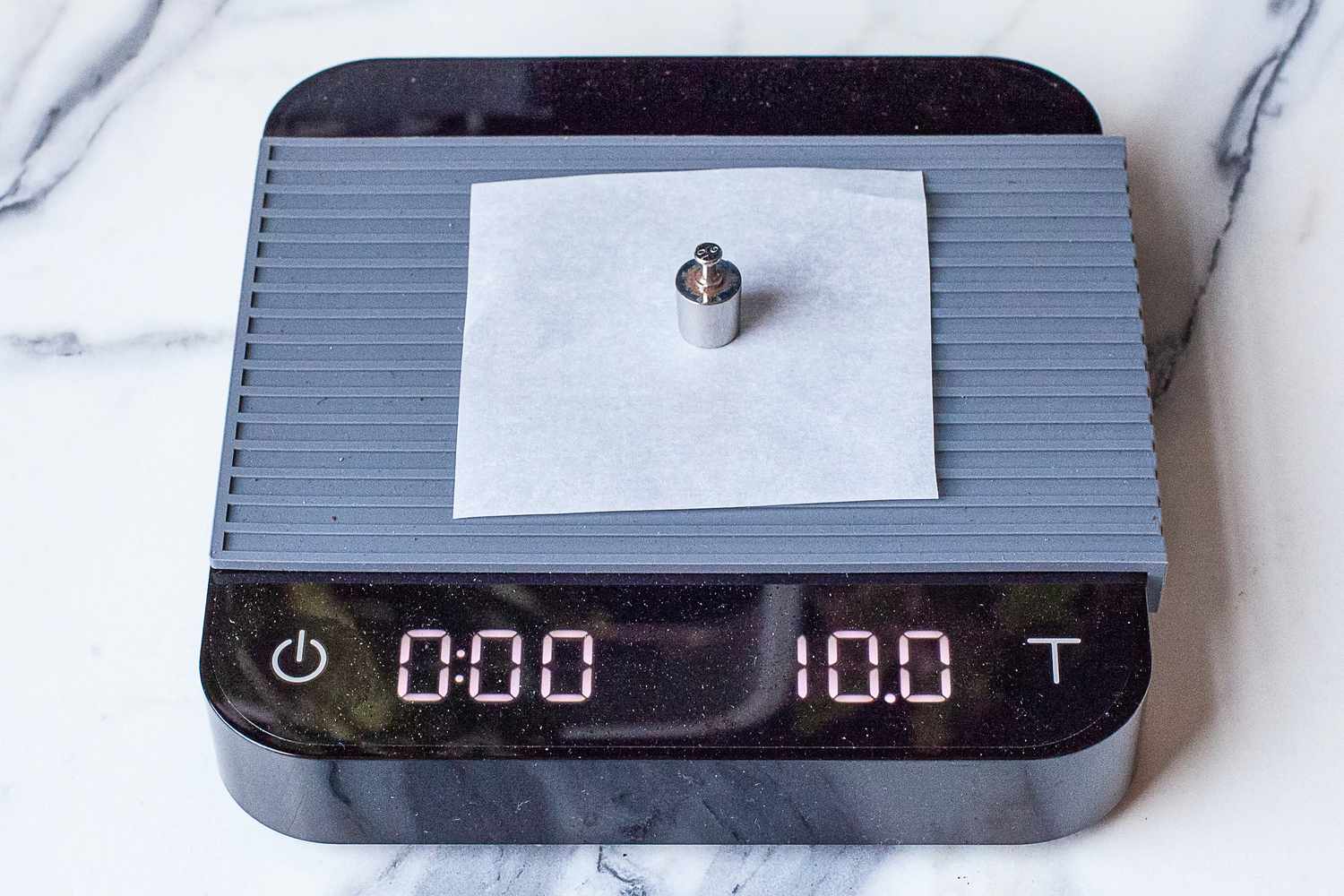 A small weight placed on a piece of paper atop a Acaia Pearl scale displaying 10.0