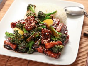Crispy tofu in a sesame seed sauce with broccoli and a bed of rice on a white plate