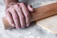 A person using a J.K. Adams Dowel Rolling Pin to flatten dough on a floured surface